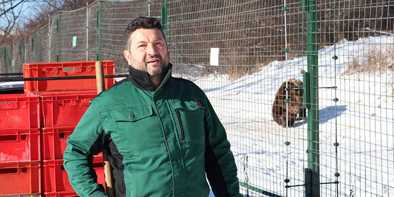 Florin stands in front of a bear enclosure covered in snow - in the distance, you can see a bear looking around.