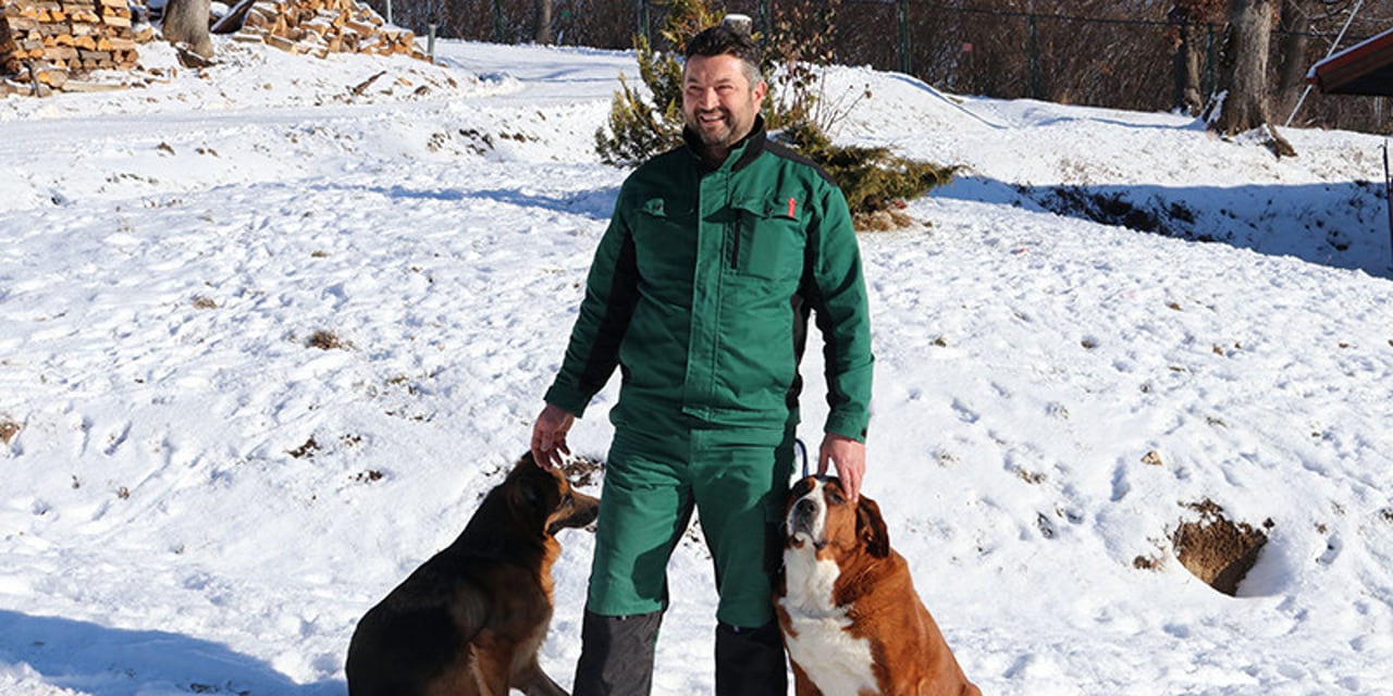 Florin wears a pair of green overalls and stands in a field covered in snow. To his left, Betty, his rescue St Bernard mix and to his right there