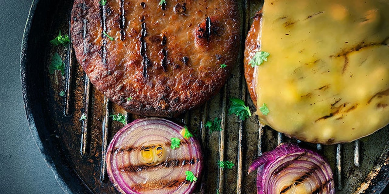 Meat-alternative burgers on a grill with cheese and onions