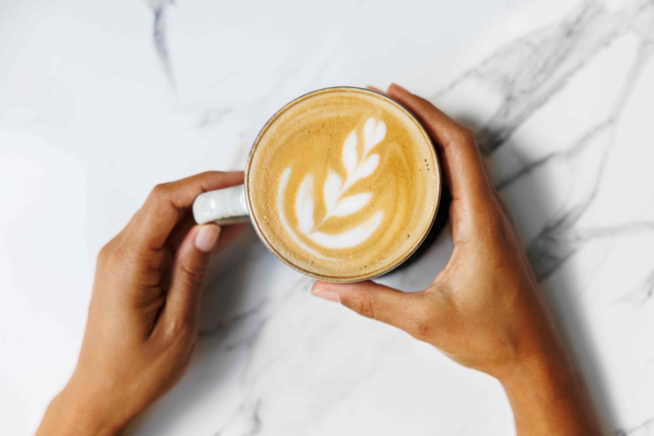 A person holding a mug that contains a latte with latte art.