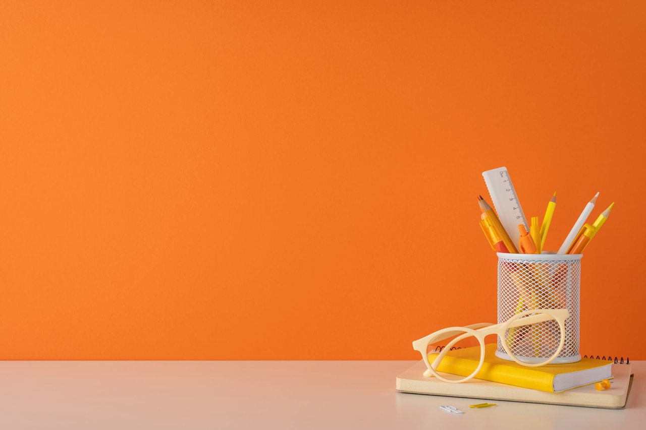 Orange background with school supplies on a desk.