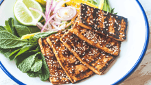 Tofu steaks on a plate with assorted veg and herbs.