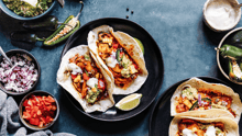 Plant-based tacos on a plate on a table with various topping surrounding them.