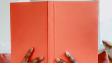 A person reading a bright orange book.