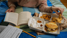 A college student eating fast food in bed while studying in their dorm.