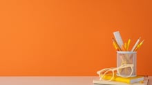 Orange background with school supplies on a desk.