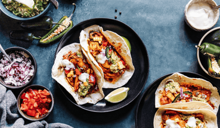 Plant-based tacos on a plate on a table with various topping surrounding them.