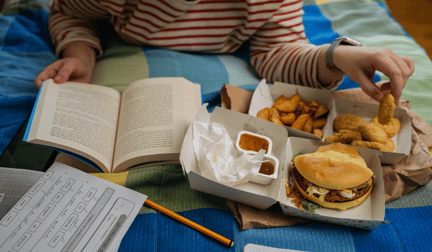 A college student eating fast food in bed while studying in their dorm.