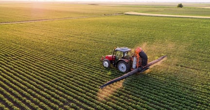 tractor spraying pesticides on a field of soybean crops