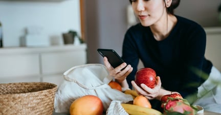 woman shopping on her phone with a bag of groceries beside her