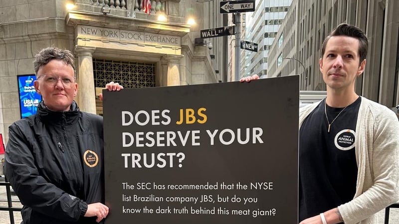 Interim US Executive Director Cameron Harsh and Global CEO Tricia Croasdell hold a sign outside of the New York Stock Exchange.