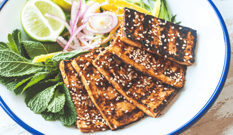Tofu steaks on a plate with assorted veg and herbs.