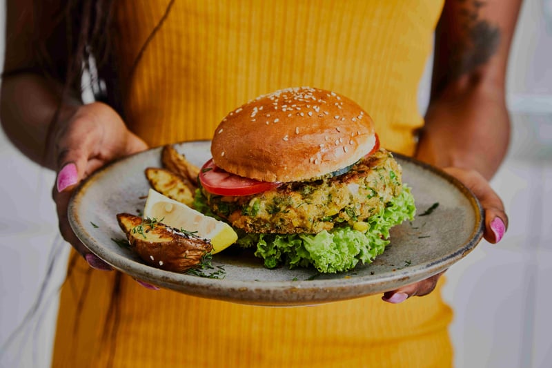A chef holding a vegan burger on a plate, presented to the camera.
