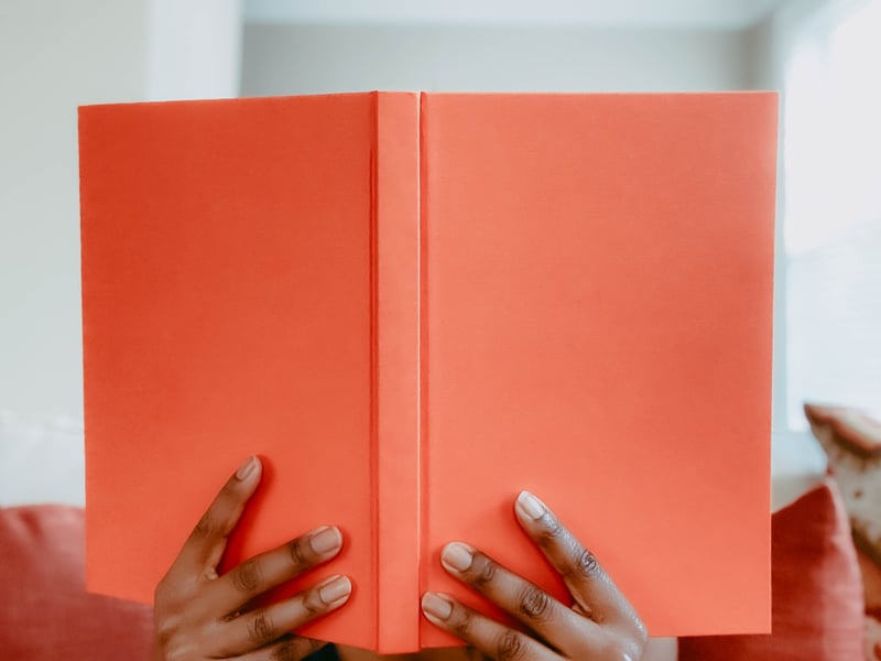 A person reading a bright orange book.