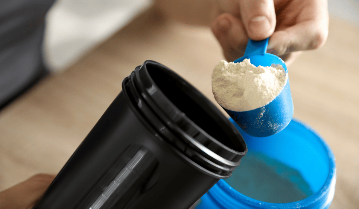 Protein powder being scooped into a bottle.